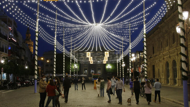 Varias personas, en el centro de la ciudad, bajo el alumbrado instalado por la semana de Feria.